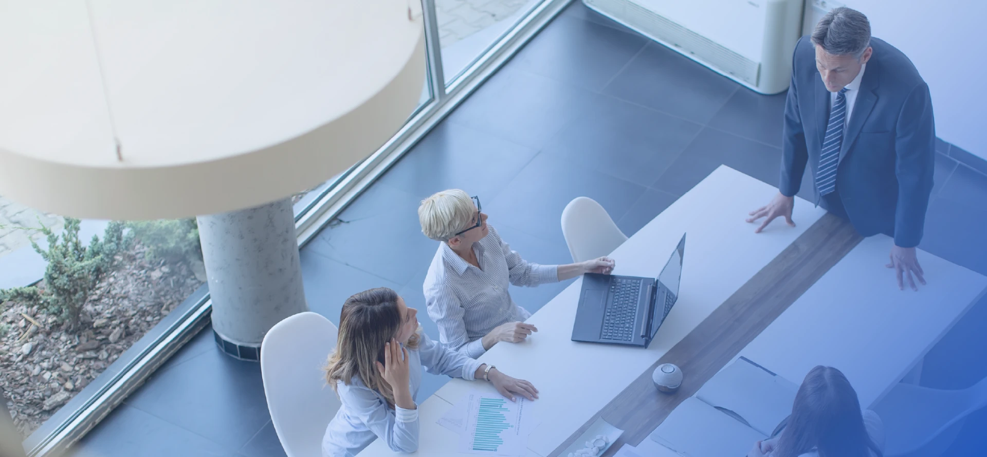 Overhead view of three business colleagues and a manager discussing charts and a laptop across a meeting table
